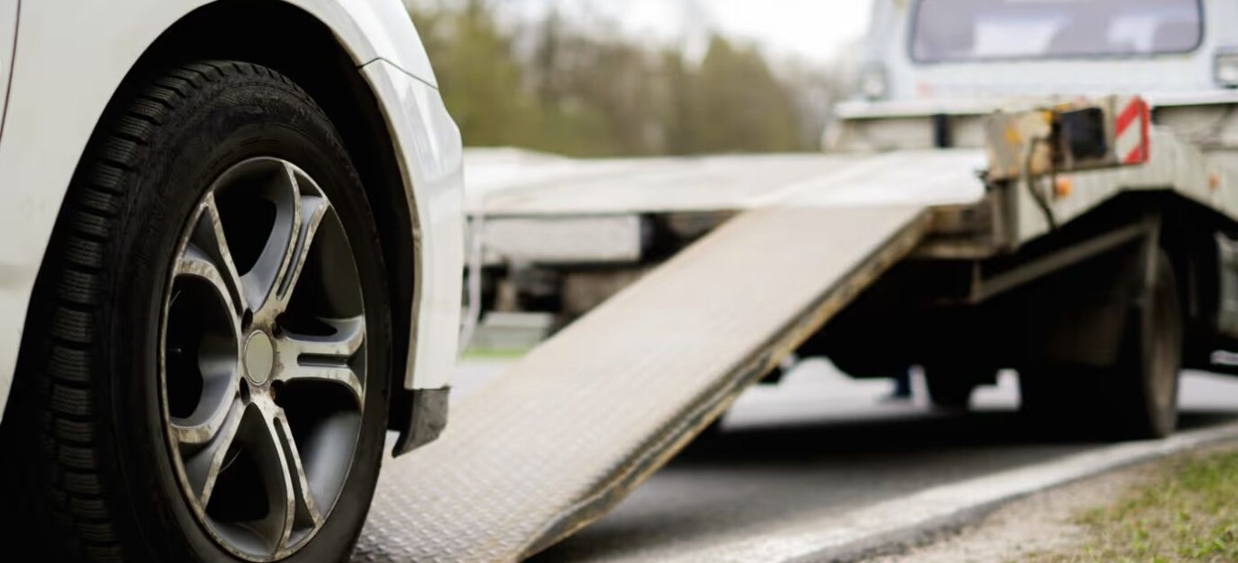 Close-up of a car wheel next to a flatbed ramp showing winch and recovery positioning in North Babylon, NY