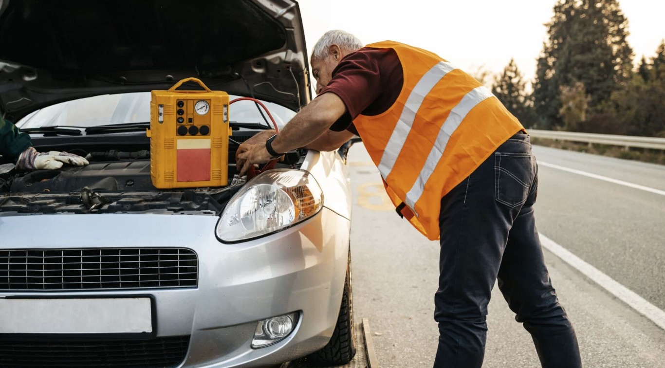 Roadside technician jump-starting a car battery on a highway near North Babylon, NY